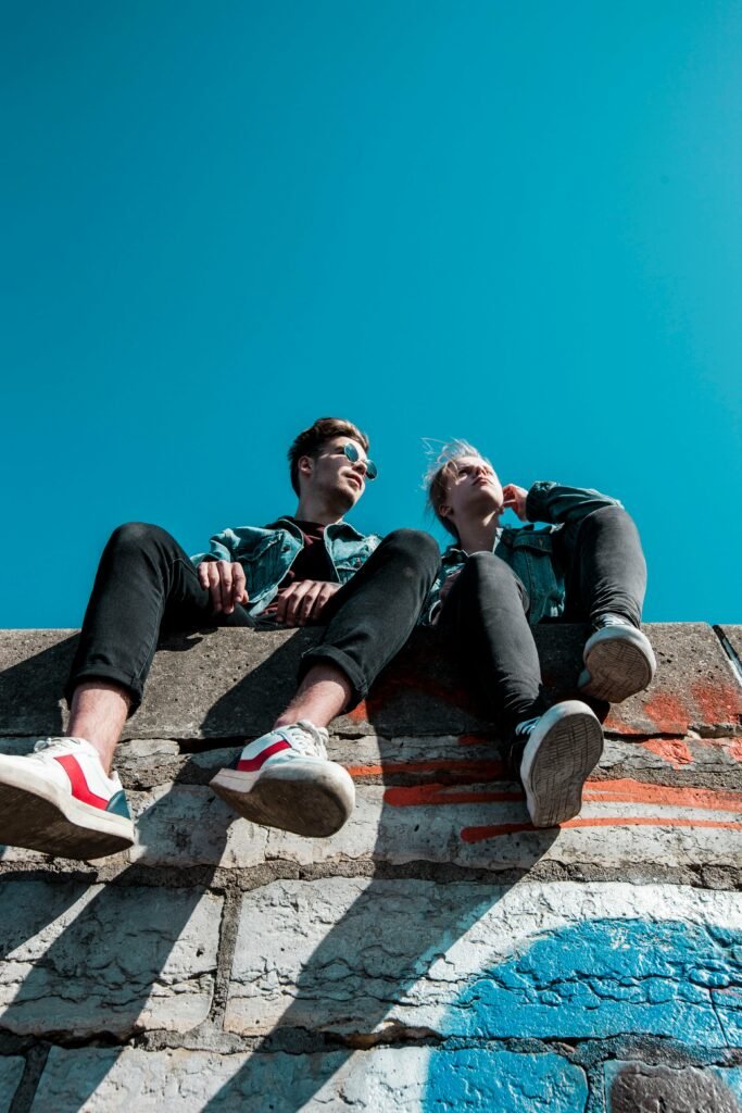 pexels-photo-1019771-1019771 Two young people sitting on a stone wall under a vibrant blue sky, enjoying a sunny day together.